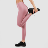 A person wearing high-waisted pink leggings and black athletic shoes, performing a standing quad stretch by holding one foot behind them against a plain gray background