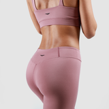 a back view for fit  woman  wearing matching bra and legging pink with loo black ,plus the background is light grey 