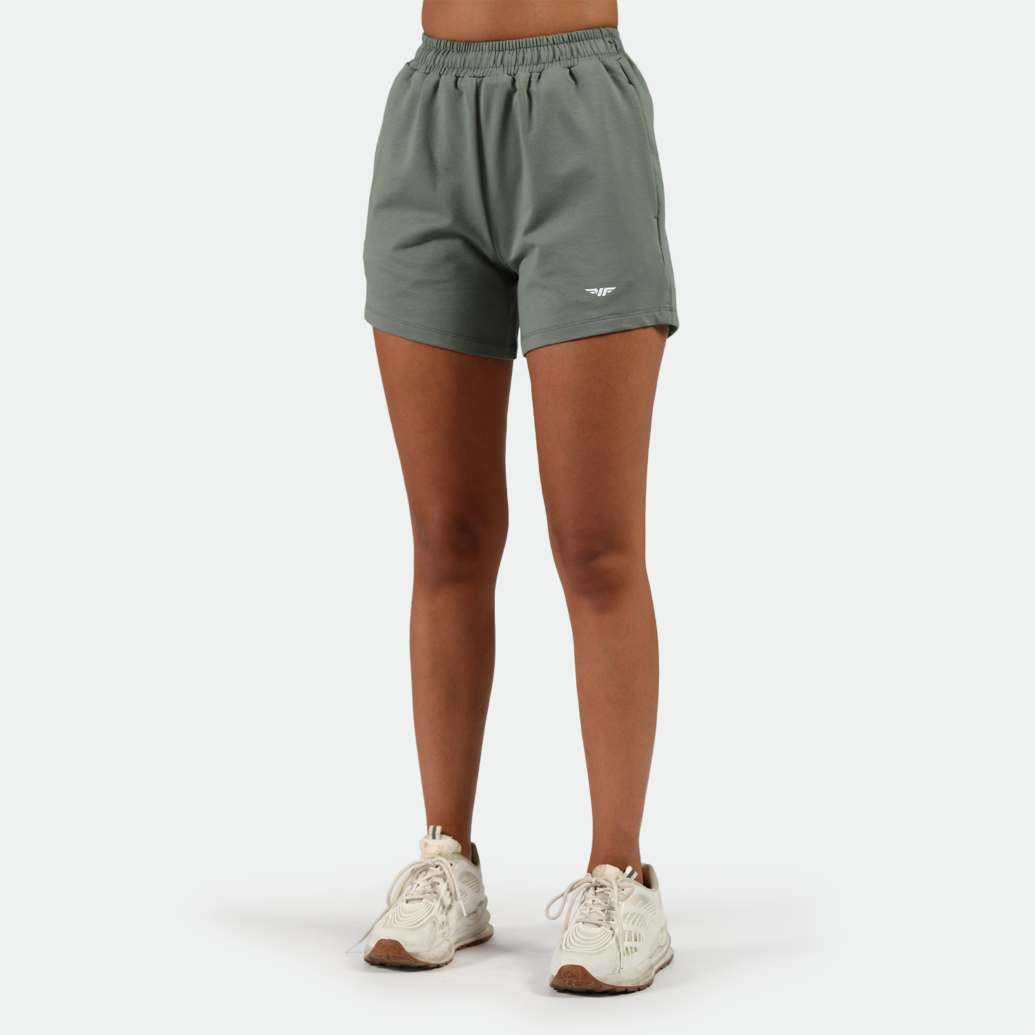 a fit woman wearing agave green short with logo and she wearing shoes white ,plus the background is light grey 