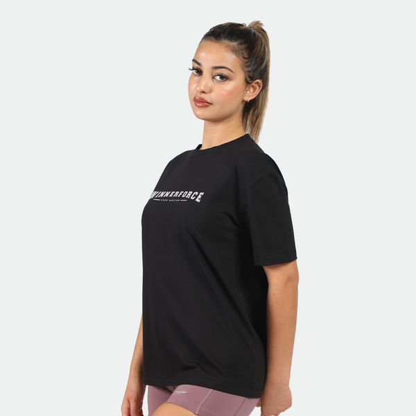 a fit woman stand at right and wearing t-shirt black with logo and she wearing purple short 