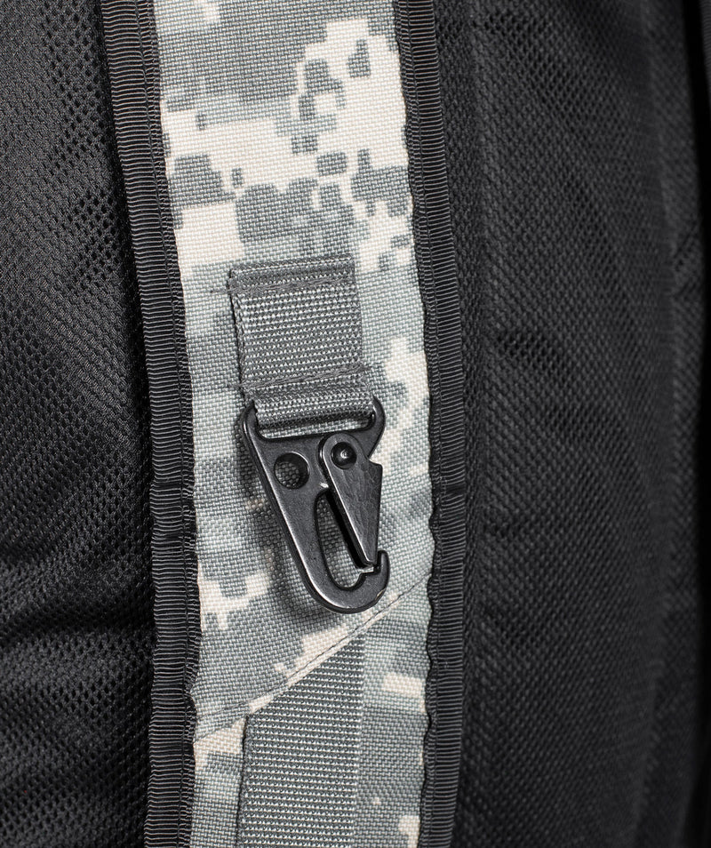 Close-up of a black backpack with a digital camouflage strap and a metal hook fastener attached to the strap. The fabric appears textured and durable.