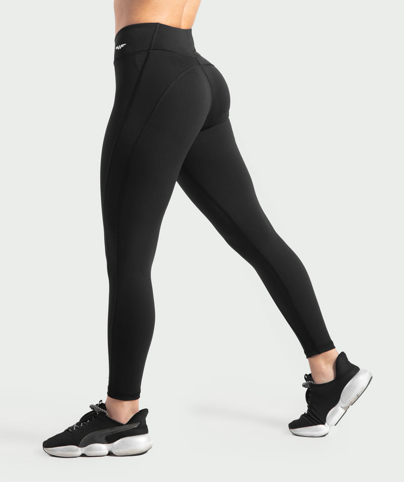 a fit woman stand at right and wearing legging black with logo white  ,she wearing shoes black , plus the background is light grey 